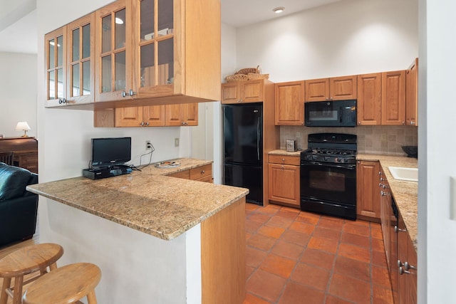 kitchen with a peninsula, black appliances, a breakfast bar area, decorative backsplash, and glass insert cabinets