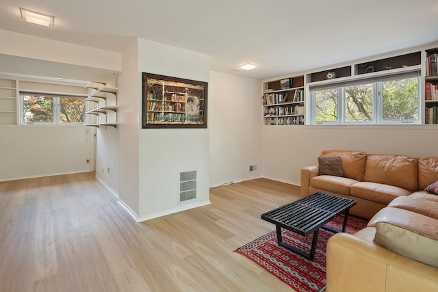 living room featuring built in shelves, baseboards, visible vents, and wood finished floors