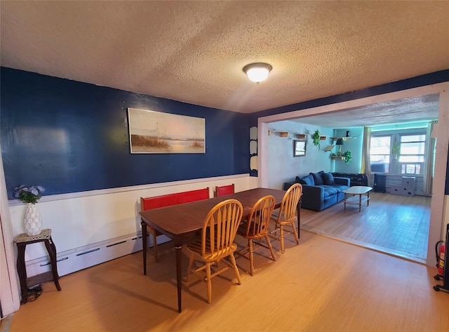 108 Main St, Livingston Manor, NY 12758 - dining area featuring wood finished floors, a textured ceiling, a wainscoted wall, and a baseboard radiator