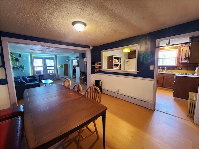 108 Main St, Livingston Manor, NY 12758 - dining space with baseboard heating, a textured ceiling, light wood-style flooring, a wainscoted wall, and plenty of natural light