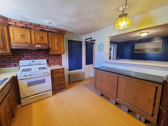 108 Main St, Livingston Manor, NY 12758 - kitchen with radiator heating unit, white gas range, under cabinet range hood, brown cabinets, and a textured ceiling