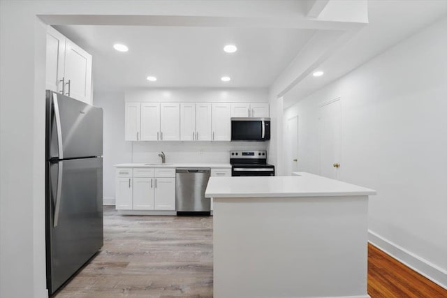 kitchen featuring stainless steel appliances, light countertops, a sink, light wood-style floors, and white cabinetry