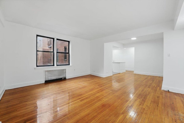 spare room featuring radiator heating unit, baseboards, and light wood-style floors