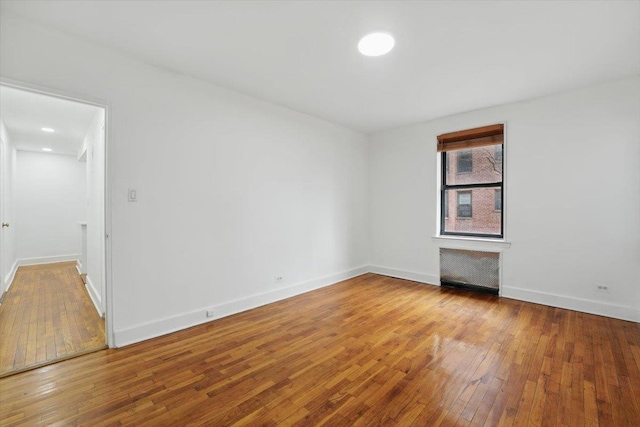 unfurnished room featuring radiator, baseboards, and hardwood / wood-style flooring