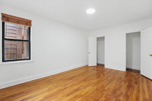unfurnished bedroom with multiple closets, baseboards, and wood finished floors