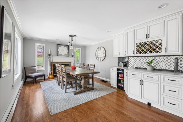 dining area featuring beverage cooler, ornamental molding, a healthy amount of sunlight, a baseboard heating unit, and bar area