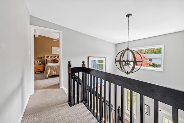 corridor featuring an inviting chandelier, carpet, plenty of natural light, and an upstairs landing
