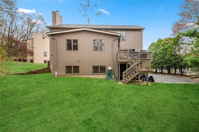 rear view of property featuring a wooden deck, a chimney, stairs, a shingled roof, and a lawn