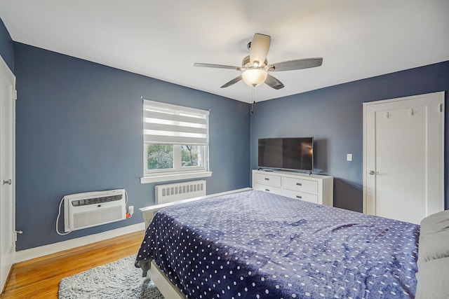 bedroom featuring a ceiling fan, wood finished floors, a wall mounted AC, radiator, and baseboards