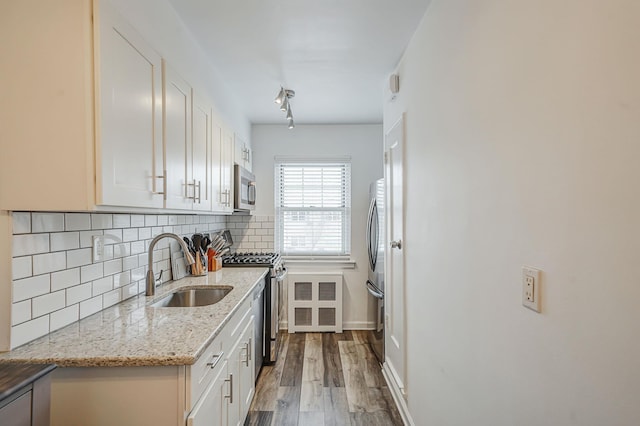 kitchen featuring white cabinets, stainless steel appliances, a sink, tasteful backsplash, and wood finished floors