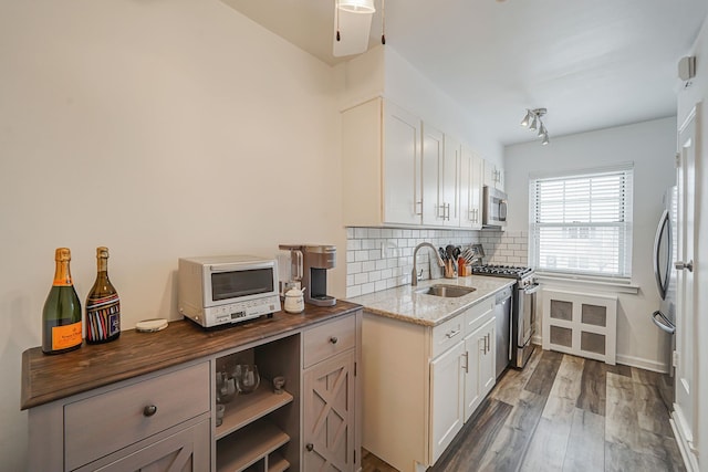 kitchen featuring backsplash, wood finished floors, a sink, dark stone counters, and appliances with stainless steel finishes