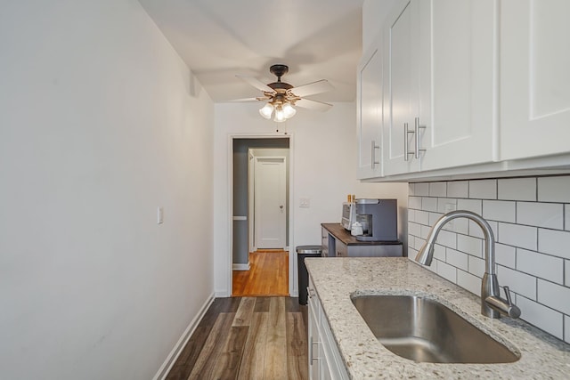 kitchen with ceiling fan, a sink, light stone countertops, tasteful backsplash, and dark wood-style flooring