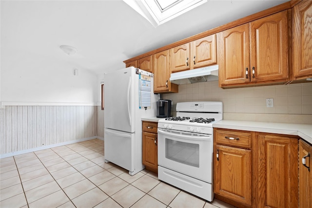 kitchen with brown cabinets, under cabinet range hood, white appliances, and a skylight