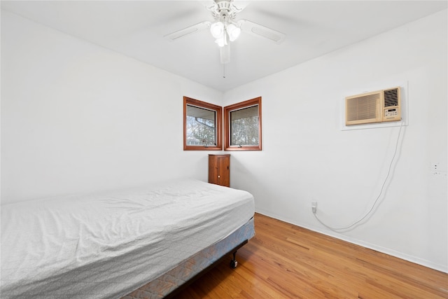 bedroom with a ceiling fan, wood finished floors, and a wall unit AC