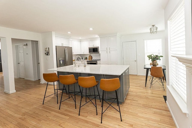 kitchen featuring a large island, backsplash, light wood-type flooring, appliances with stainless steel finishes, and white cabinetry