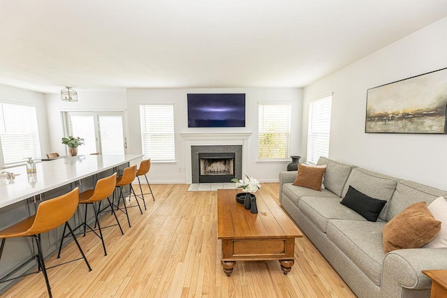 living area with a high end fireplace, baseboards, light wood-type flooring, and plenty of natural light