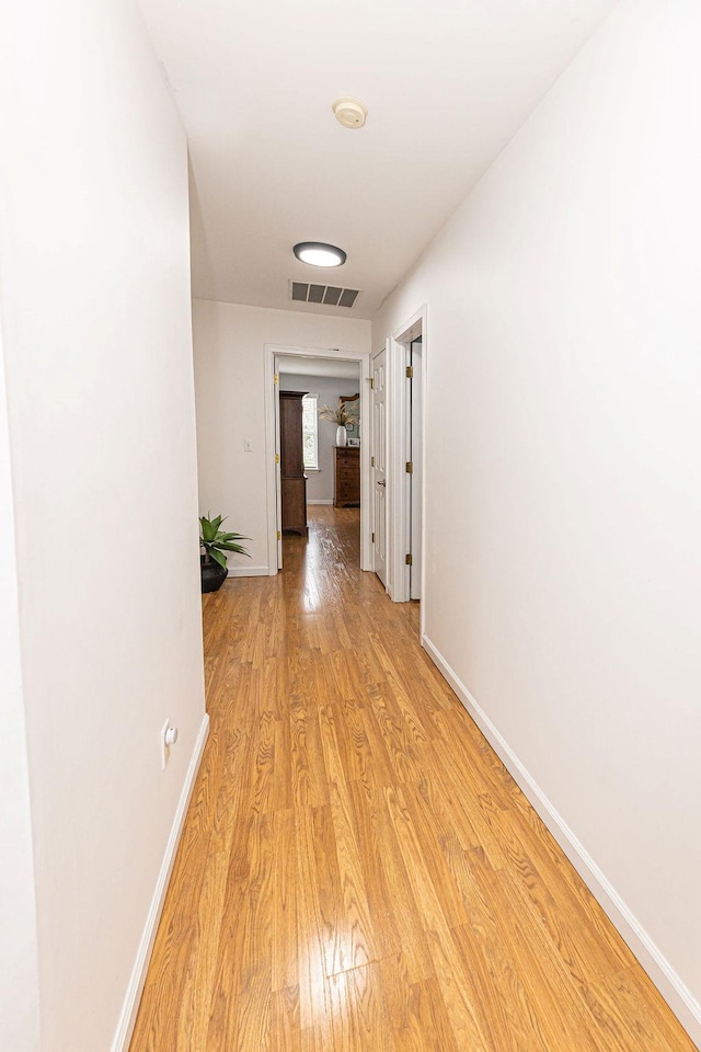 hall with baseboards, visible vents, and light wood-style flooring