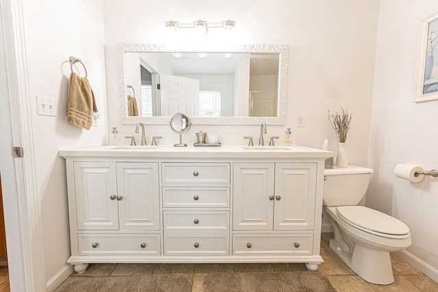 bathroom featuring baseboards, a sink, double vanity, and toilet