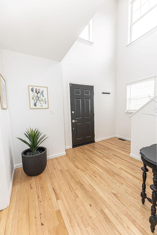 entryway with visible vents, light wood finished floors, baseboards, and a towering ceiling
