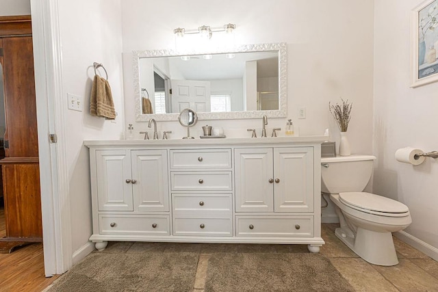 bathroom with double vanity, toilet, baseboards, and a sink