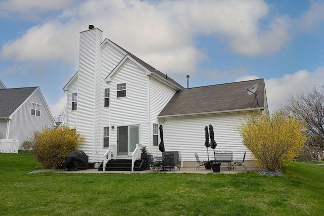 back of house featuring entry steps, a lawn, a patio, and a chimney