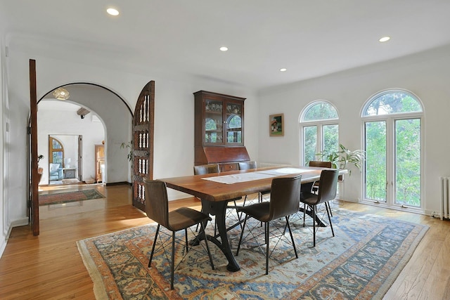 dining space with light wood-style floors, arched walkways, recessed lighting, and radiator