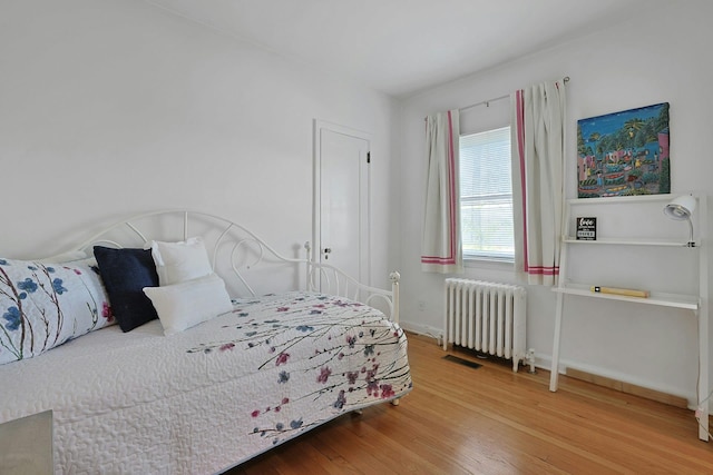 bedroom featuring baseboards, visible vents, radiator heating unit, and wood finished floors