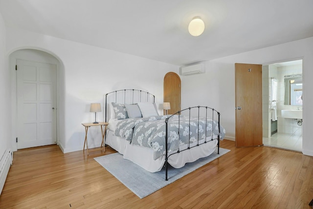 bedroom with arched walkways, baseboards, a wall mounted AC, and light wood finished floors