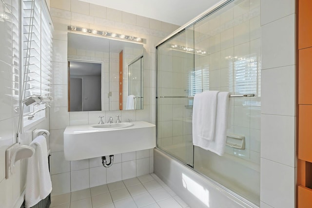bathroom featuring enclosed tub / shower combo, tile patterned floors, tile walls, and a sink