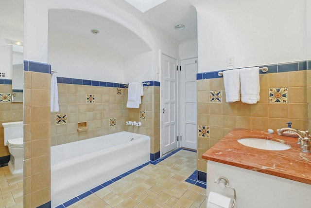 full bath with vanity, toilet, a wainscoted wall, tile walls, and a garden tub