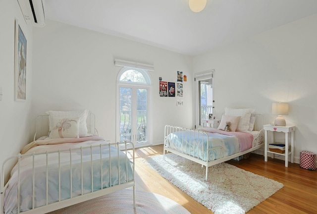 bedroom with an AC wall unit, access to exterior, and wood finished floors