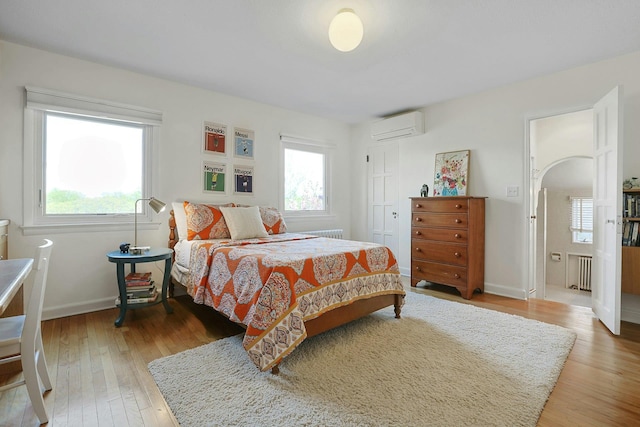 bedroom featuring a wall mounted air conditioner, baseboards, a closet, light wood finished floors, and radiator