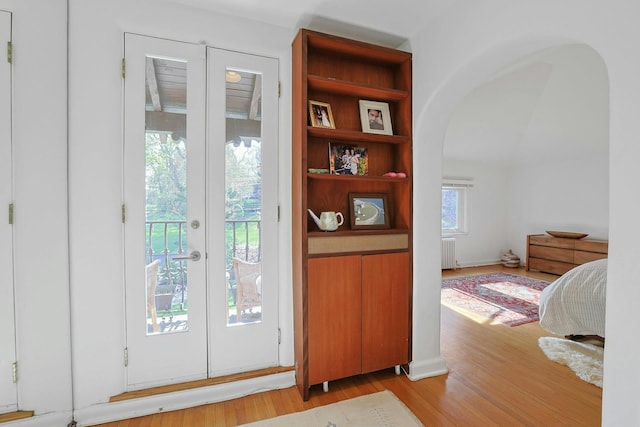 entryway featuring arched walkways, french doors, radiator, and light wood-type flooring