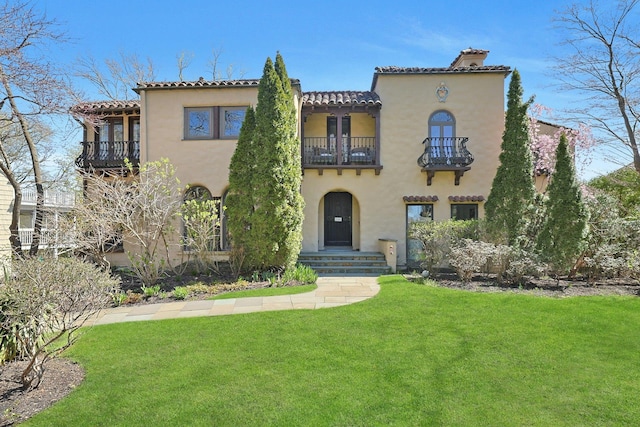 mediterranean / spanish-style home featuring a front lawn, stucco siding, a chimney, a balcony, and a tiled roof