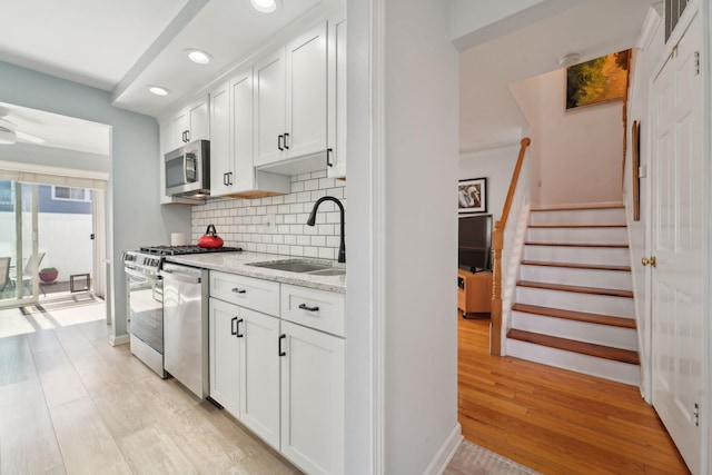 kitchen with white cabinets, tasteful backsplash, a sink, light wood-style flooring, and appliances with stainless steel finishes
