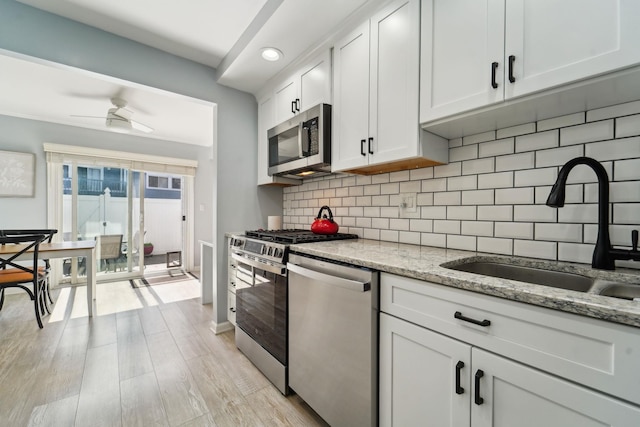 kitchen featuring decorative backsplash, appliances with stainless steel finishes, a sink, white cabinets, and light wood-style flooring