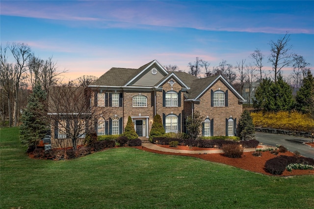 colonial inspired home featuring a lawn and brick siding