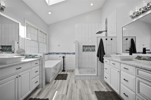 bathroom with walk in shower, vaulted ceiling with skylight, a soaking tub, and a sink