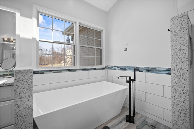 bathroom featuring vanity, wainscoting, a freestanding tub, and tile walls