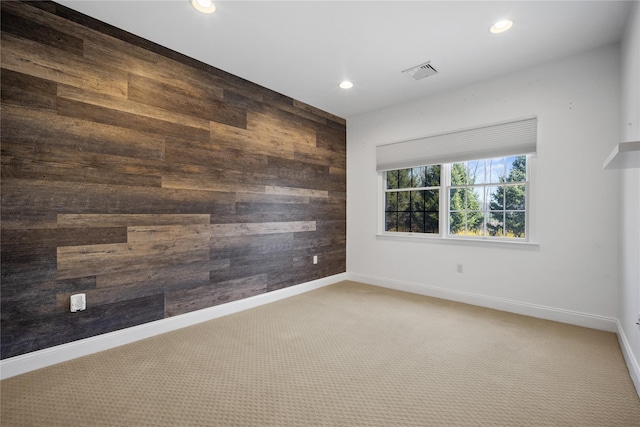 carpeted spare room featuring baseboards, visible vents, wooden walls, and recessed lighting