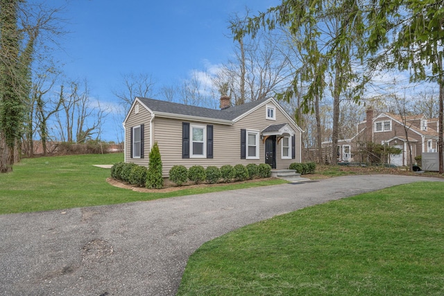 view of front of house with driveway, a chimney, and a front lawn
