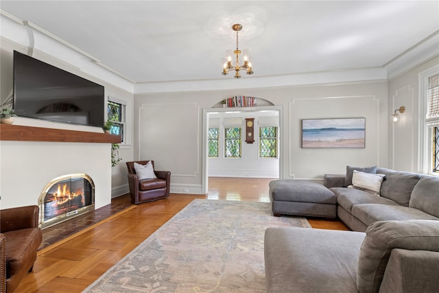 living room with crown molding, baseboards, a chandelier, and a glass covered fireplace