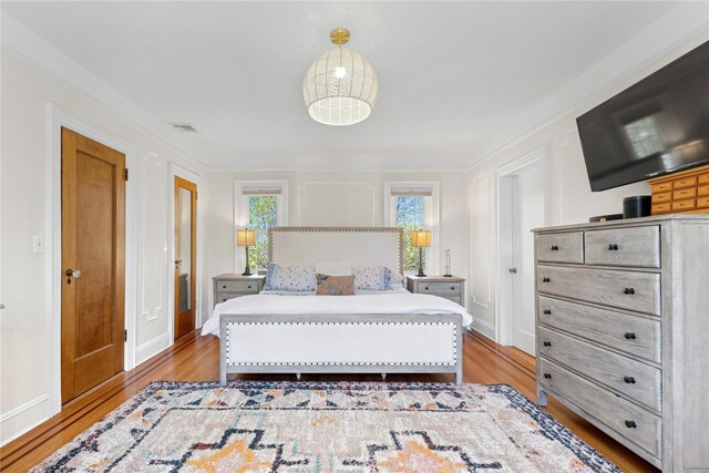 bedroom with visible vents, baseboards, crown molding, and wood finished floors