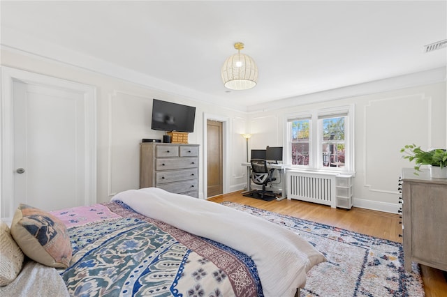 bedroom featuring radiator heating unit, baseboards, wood finished floors, and visible vents
