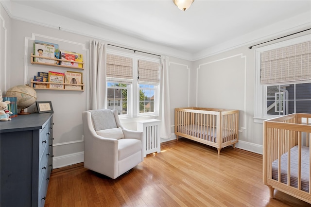 bedroom with baseboards, a crib, and light wood-type flooring