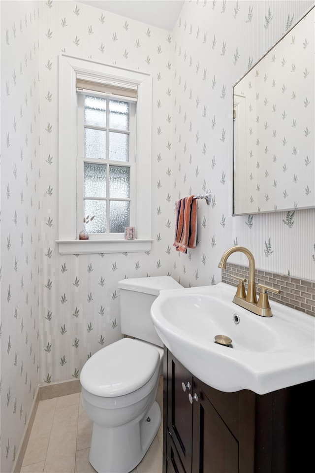 half bath featuring tile patterned flooring, vanity, baseboards, toilet, and wallpapered walls