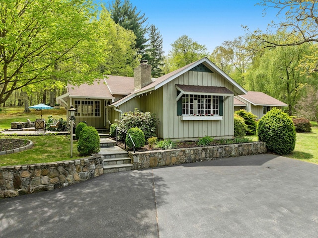 view of front facade with a chimney, board and batten siding, a patio area, roof with shingles, and a front lawn