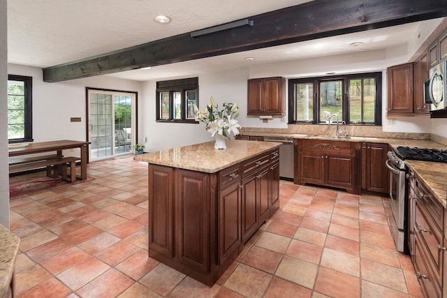 kitchen featuring light stone countertops, a sink, a kitchen island, beamed ceiling, and appliances with stainless steel finishes
