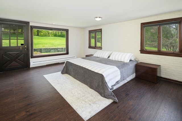 bedroom featuring multiple windows, baseboard heating, hardwood / wood-style floors, and brick wall