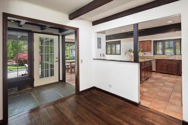 kitchen featuring a sink, light wood finished floors, beamed ceiling, baseboards, and dark countertops